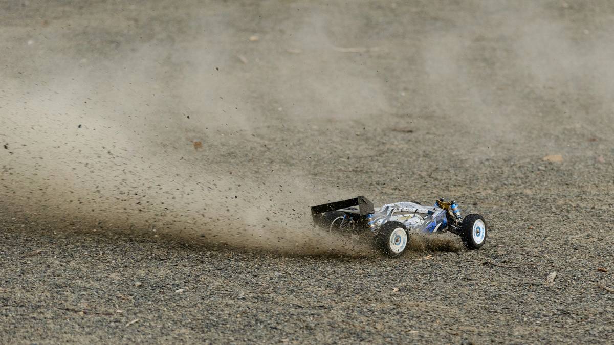 Crowd of enthusiasts at rc car racing events cheering as cars speed around an outdoor dirt track